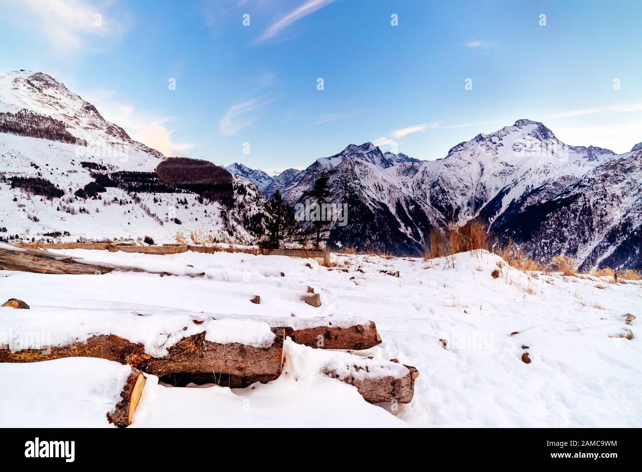 Vista dalla periferia di Les deux Alpes villaggio sulla catena montuosa con tronchi d'albero coperti di neve. Tramonto sulle alpi francesi, regione del Rodano-Alvernia, Francia Foto Stock