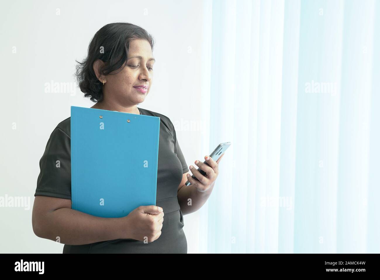 Donna aziendale indiana intelligente e bella con un file blu che texting sul suo telefono. Foto Stock