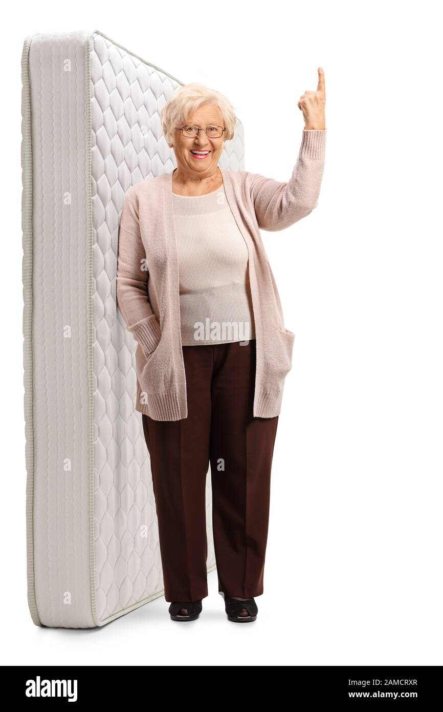 Ritratto a tutta lunghezza di una signora anziana appoggiata su un materasso del letto e che punta su isolato su sfondo bianco Foto Stock
