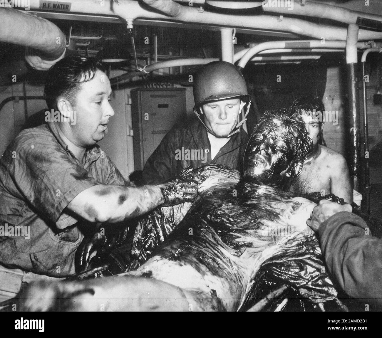 I marinai della marina statunitense si rilassano mentre i due guardsmen della costa raschiano un rivestimento spesso di olio dal suo corpo. La nave sopravvissuta, la USS LANSDALE, fu affondata da aerei nazisti al largo della costa del Nord Africa. Aprile 1944 Foto Stock