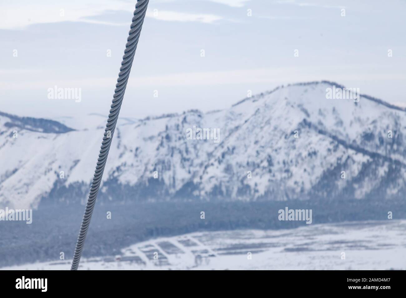 Un cavo metallico da uno skilift ad un'altezza con uno sfondo di montagne innevate Altai. Arrampicata e costruzione di roccia. Foto Stock