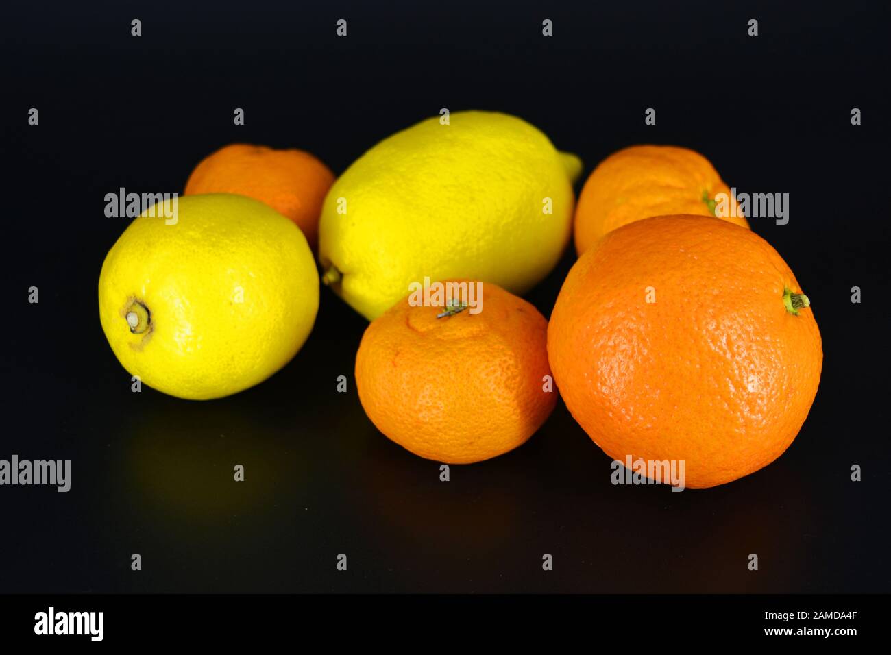 Frutta fresca e brillante, due limoni gialli, tre piccoli mandarini arancioni, una grande mineralola si trova su uno sfondo di plastica nera. Delizioso e dolce. Foto Stock