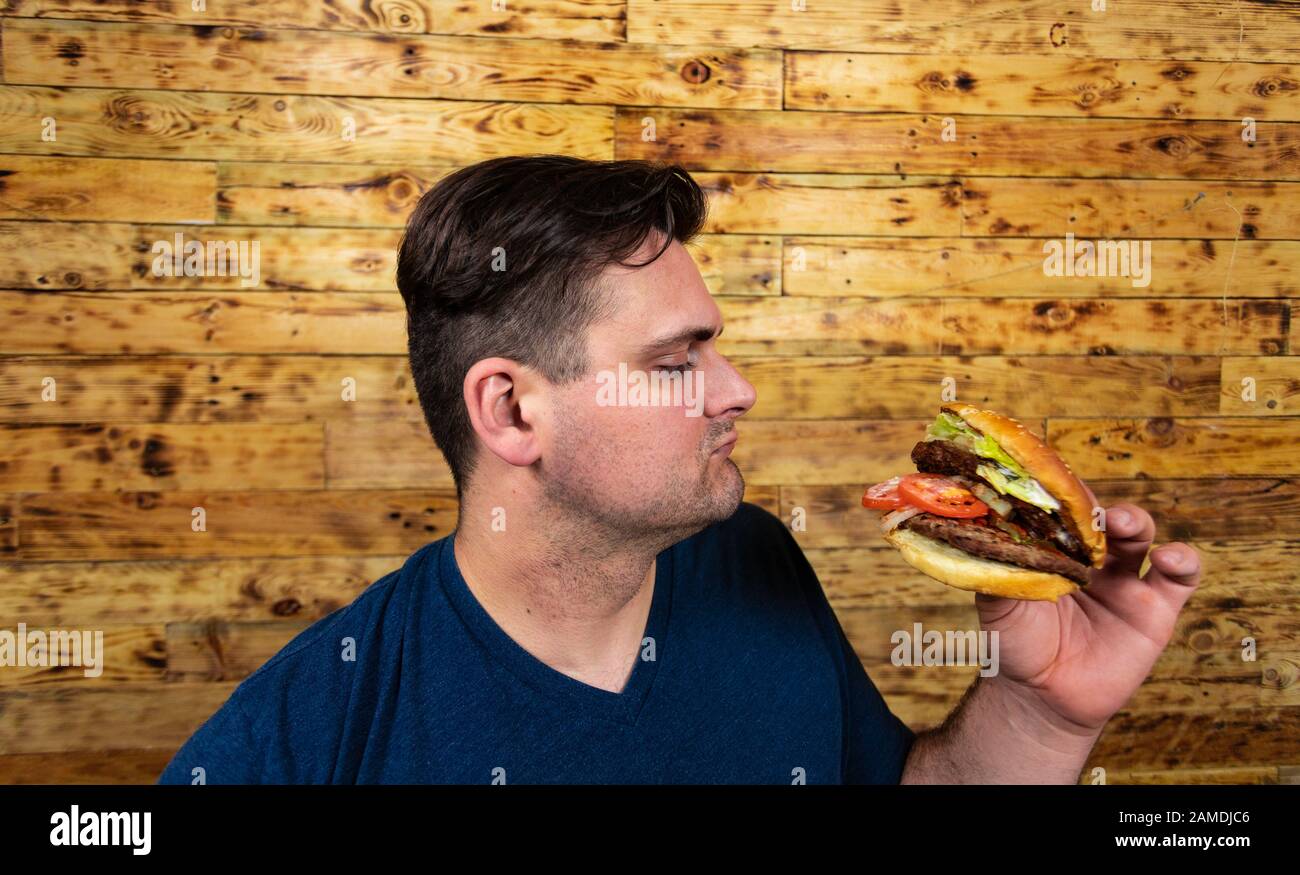 Giovane bell'uomo sta posando con il suo hamburger gustoso e sta per goderlo. Foto Stock