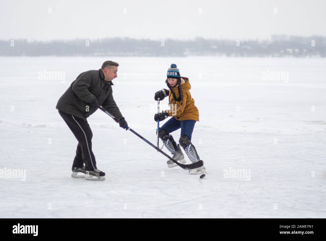 Dnipro, Ucraina - 28 gennaio 2018: Ragazza adolescente che attacca il difensore maschio mentre gioca a hockey con uomini maturi su un fiume ghiacciato Dnipro in Ucraina Foto Stock