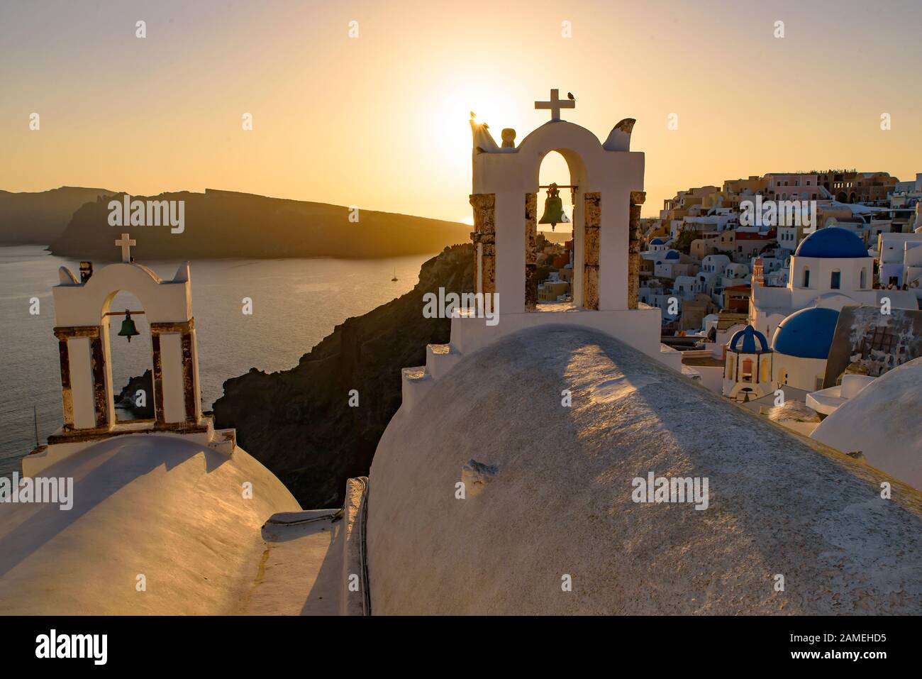 Chiese a cupola blu e campanile di fronte al Mar Egeo con calda luce del tramonto a Oia, Santorini, Grecia Foto Stock