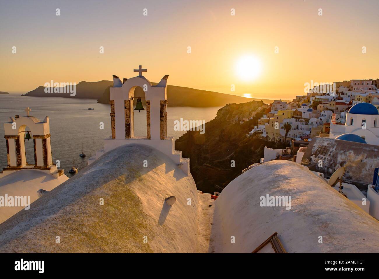 Chiese a cupola blu e campanile di fronte al Mar Egeo con calda luce del tramonto a Oia, Santorini, Grecia Foto Stock