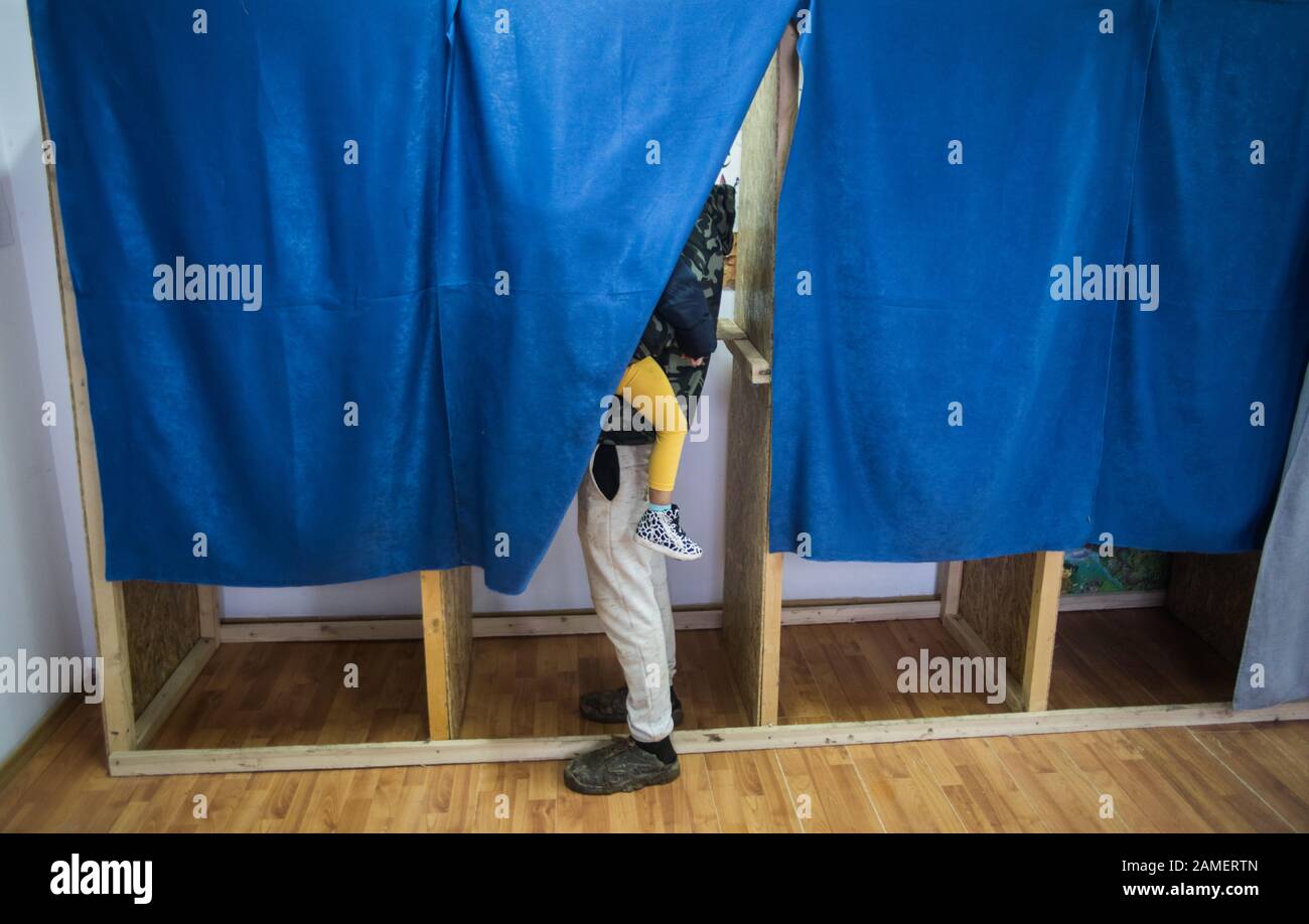Immagine a colori di una persona non identificabile che vota e tiene un bambino, in cabine presso un seggio elettorale, durante le elezioni. Foto Stock