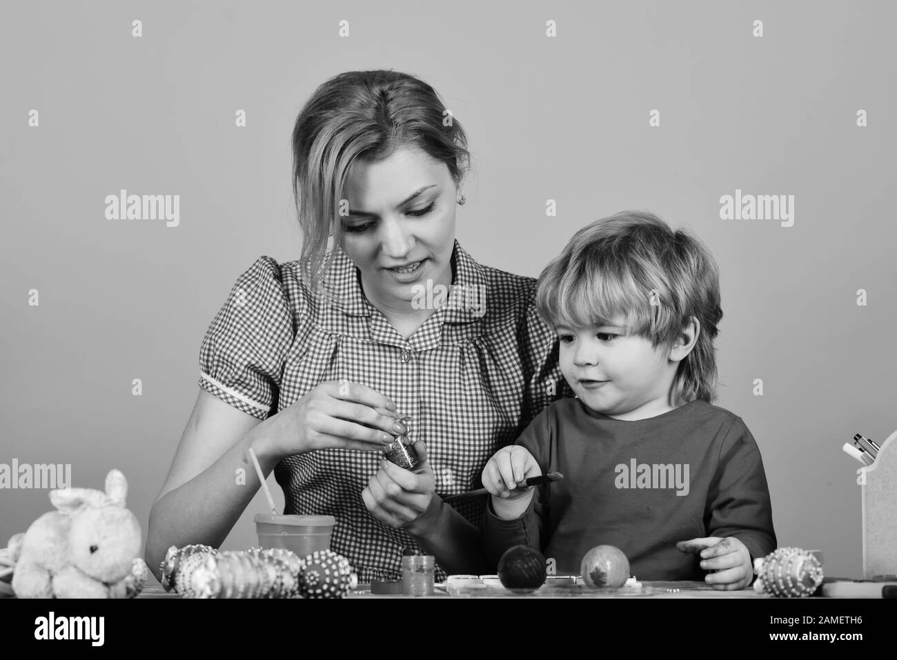 Madre e figlio che dipingano le uova per Pasqua. Pasqua e momenti felici concetto. Donna e ragazzino con volti sorridenti che fanno decorazioni. La famiglia si prepara per la vacanza su sfondo rosa. Foto Stock