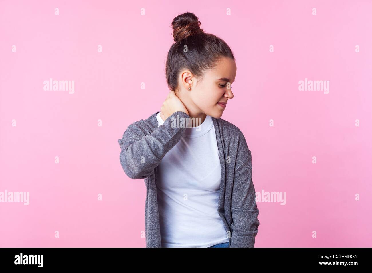 Ritratto di ragazza teen bruna stanca malsana con acconciatura di bun in vestiti casuali che massaggiano il collo dolorante e che grimacing da dolore, tensione muscolare. IND Foto Stock