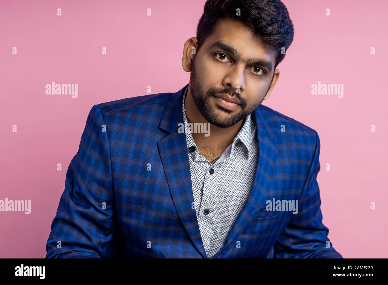 Ritratto di closeup orizzontale di bello sicuro businesslike giovane uomo d'affari indiano seduto sul posto di lavoro in ufficio, indossare camicia, abito a scacchi, Foto Stock