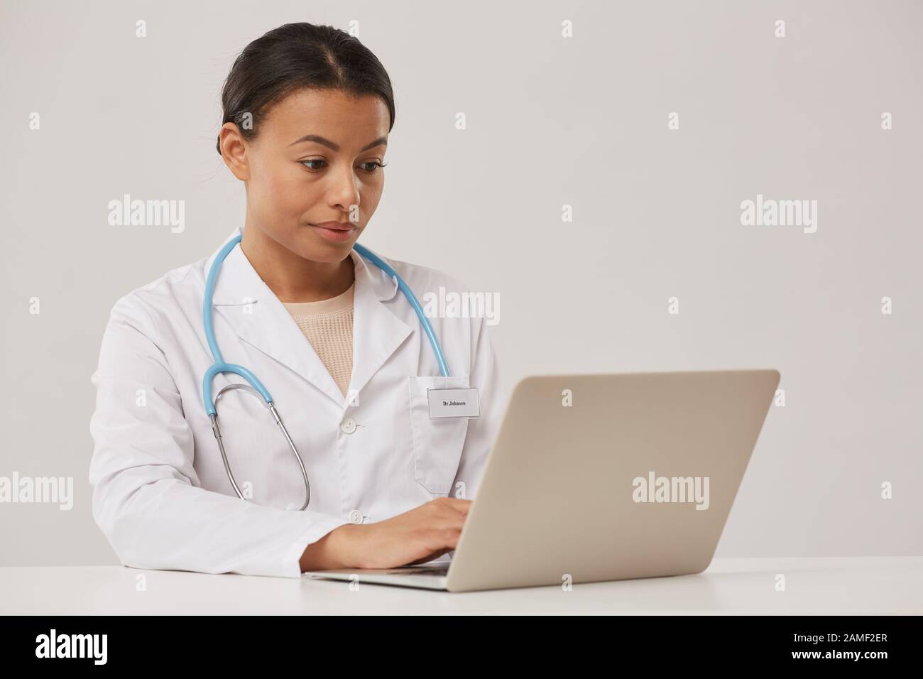 Ritratto di bella medico femminile utilizzando il computer portatile mentre seduto su sfondo bianco, copia spazio Foto Stock