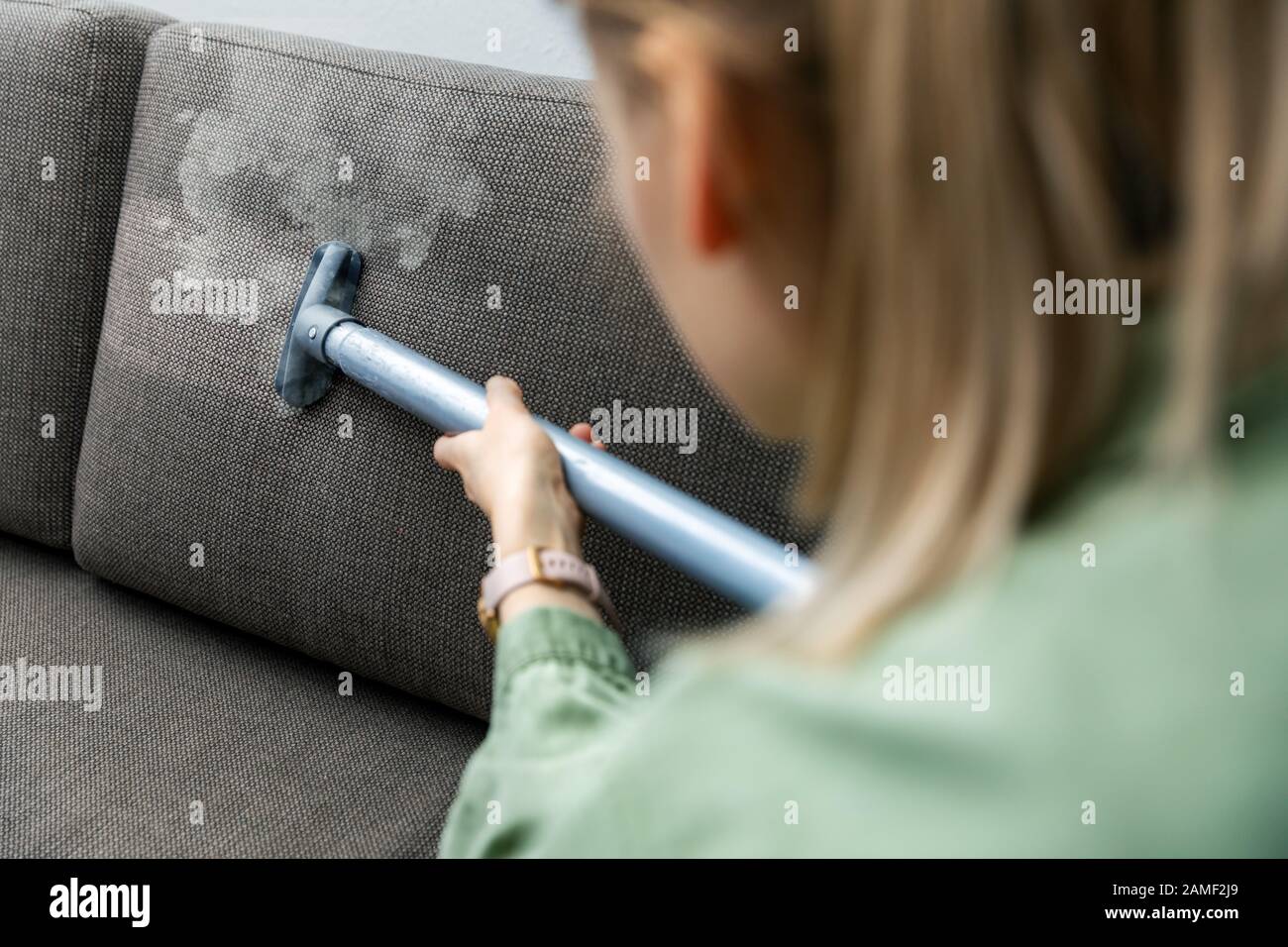 donna pulisce il divano in tessuto con un pulitore a vapore a casa Foto Stock