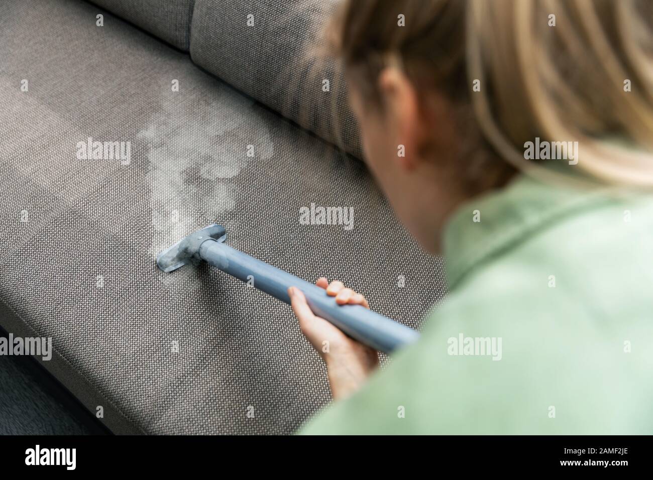 donna pulisce il divano in tessuto con un pulitore a vapore a casa Foto Stock