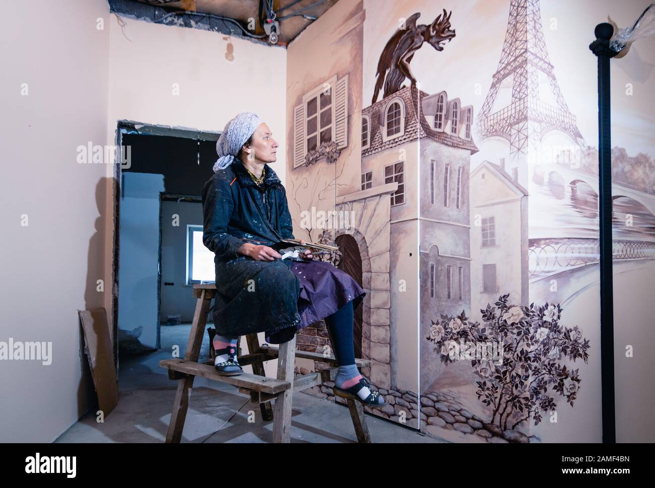 Donna artista siede contro un muro con murale in un soggiorno e guarda il suo lavoro. Il murale è dedicato alle impressioni di Parigi. Foto Stock