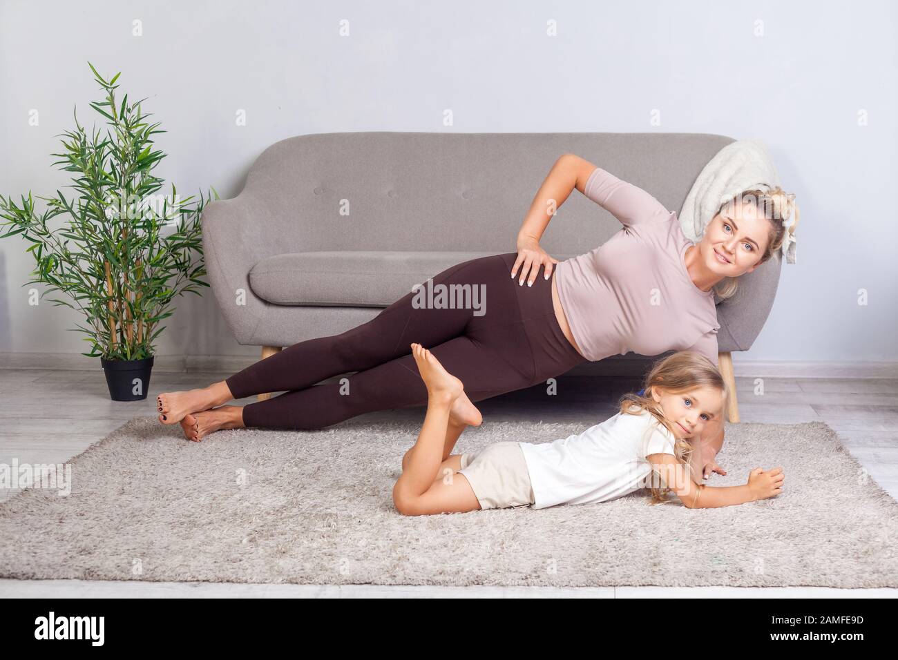 Adorabile bambino sdraiato vicino giovane attraente madre che pratica yoga, posa laterale Plank, felice famiglia facendo ginnastica insieme, allenamento fitness Foto Stock