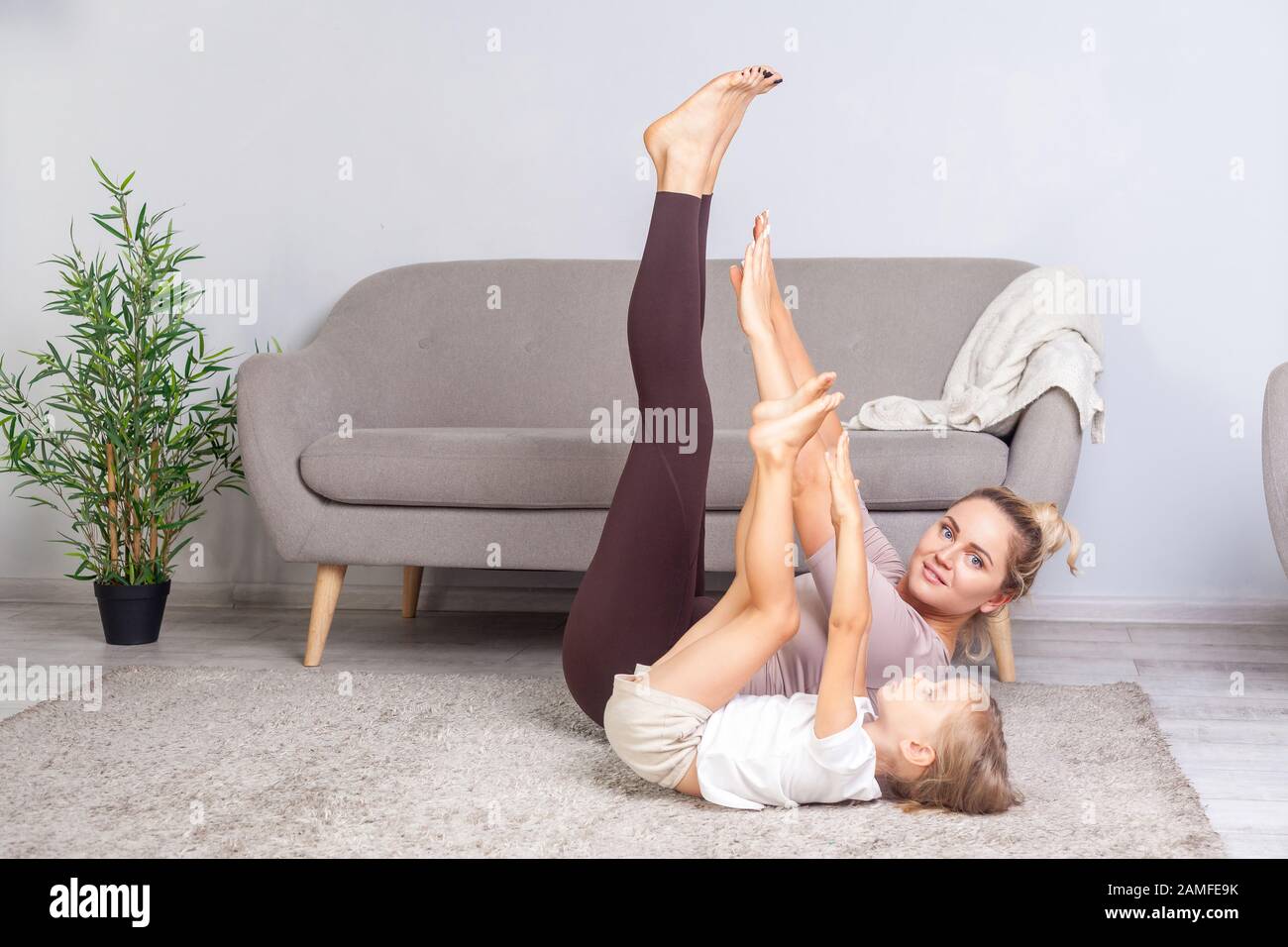 Giovane donna positiva fare esercizi di flessibilità stretching insieme con la sua figlia prescolare, felice famiglia praticando ginnastica a casa, fitness Foto Stock