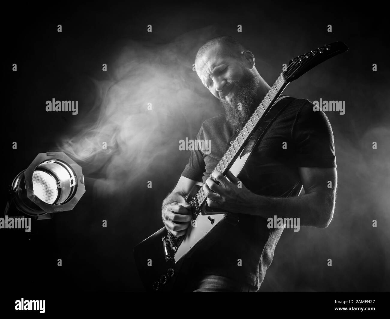 Foto di un uomo con bearded che suona la chitarra elettrica sul palco davanti ai faretti. Foto Stock