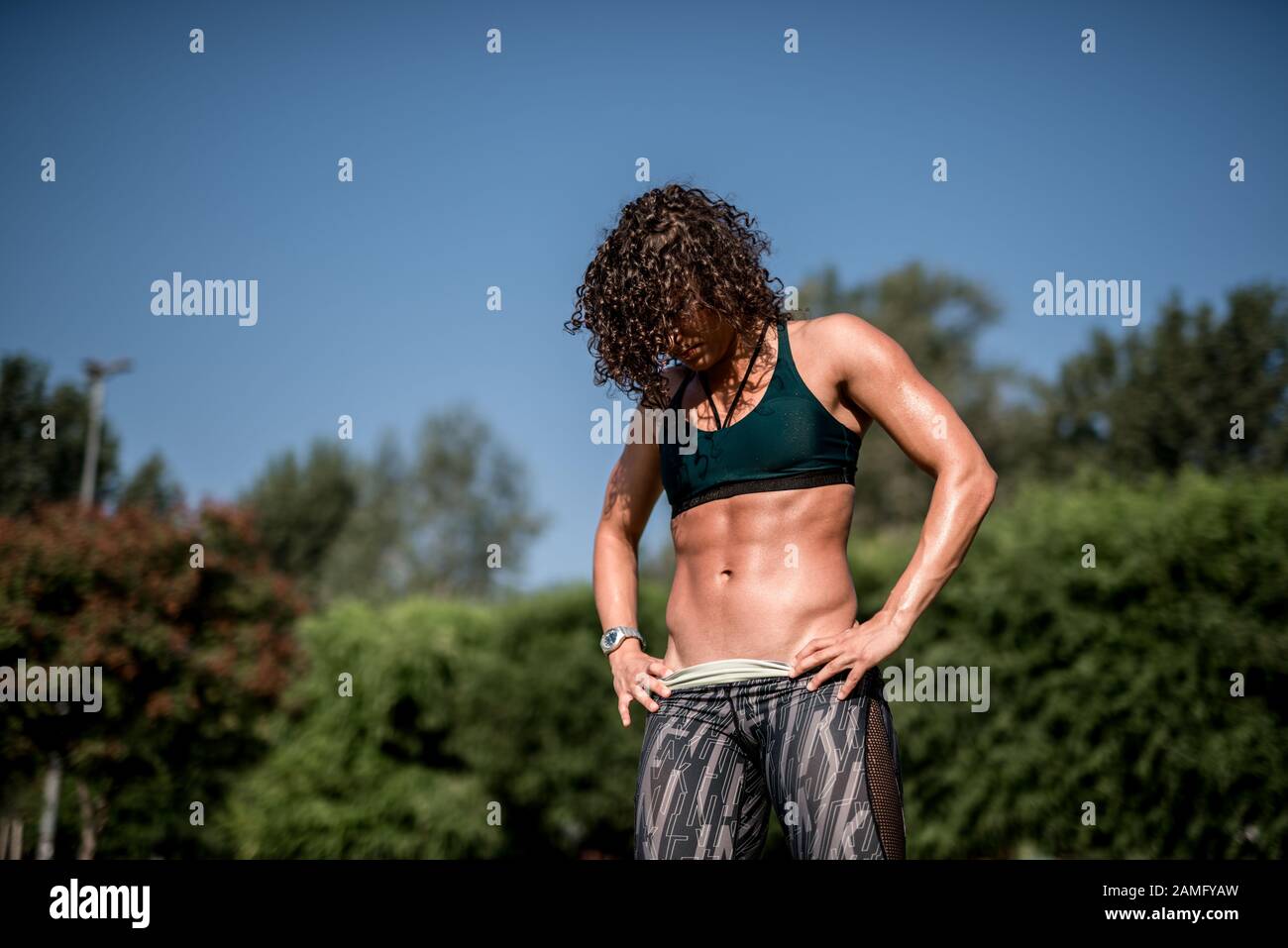 Donna atletica con forti muscoli addominali che posano con le sue mani sui fianchi in luce ombreggiata per enfatizzare il suo fisico Foto Stock