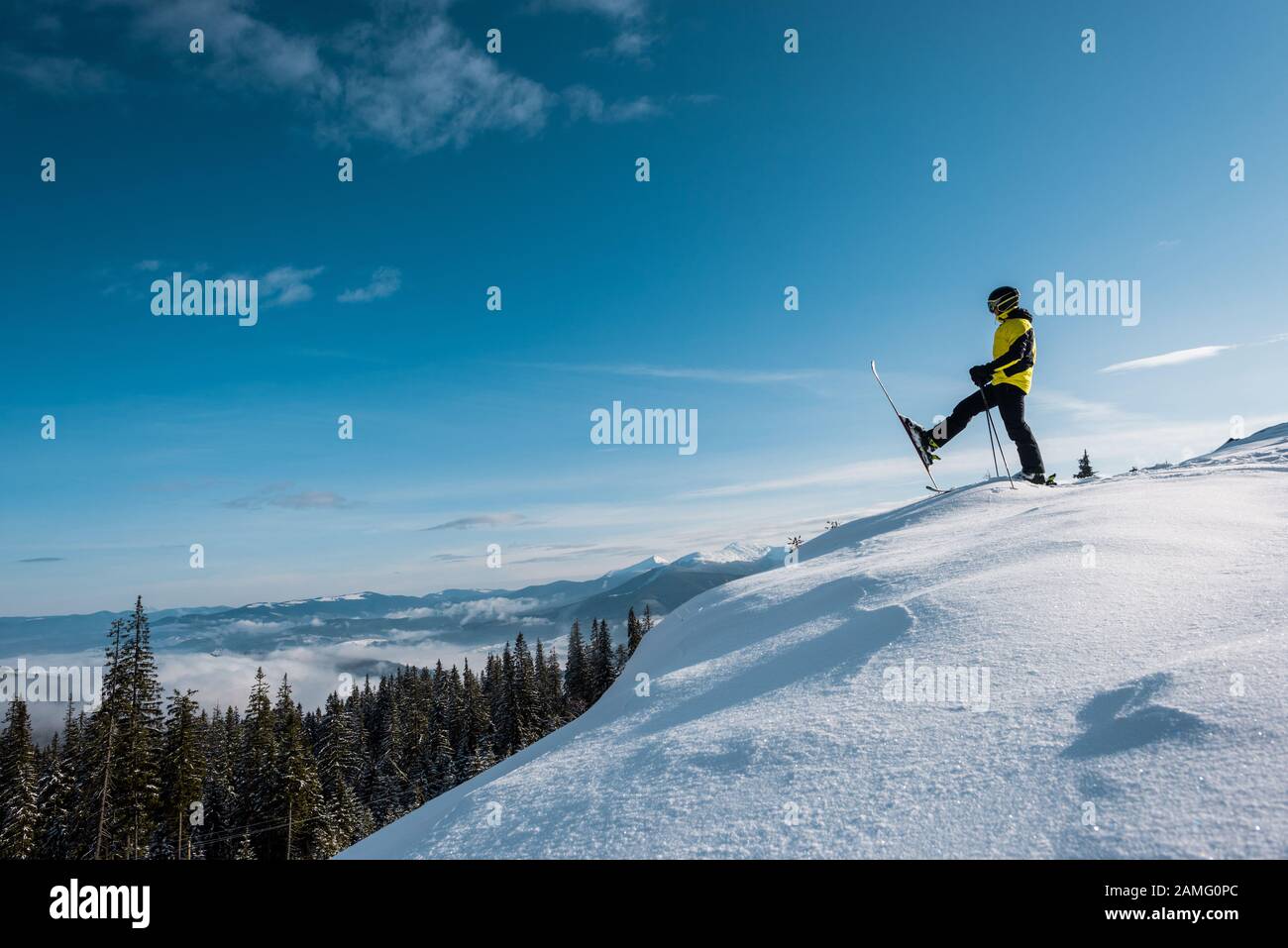 vista laterale dello sciatore che tiene gli bastoni da sci e fa un passo contro il cielo blu in montagna Foto Stock