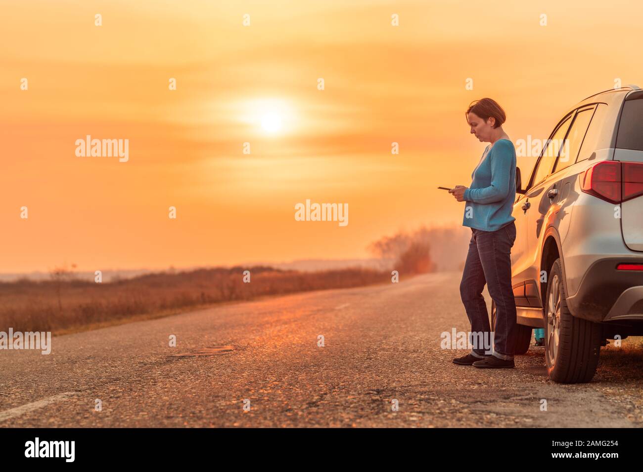 Donna di messaggistica di testo assistenza stradale aiuto dopo auto si è rotta sulla strada di campagna in autunno il tramonto, il fuoco selettivo Foto Stock