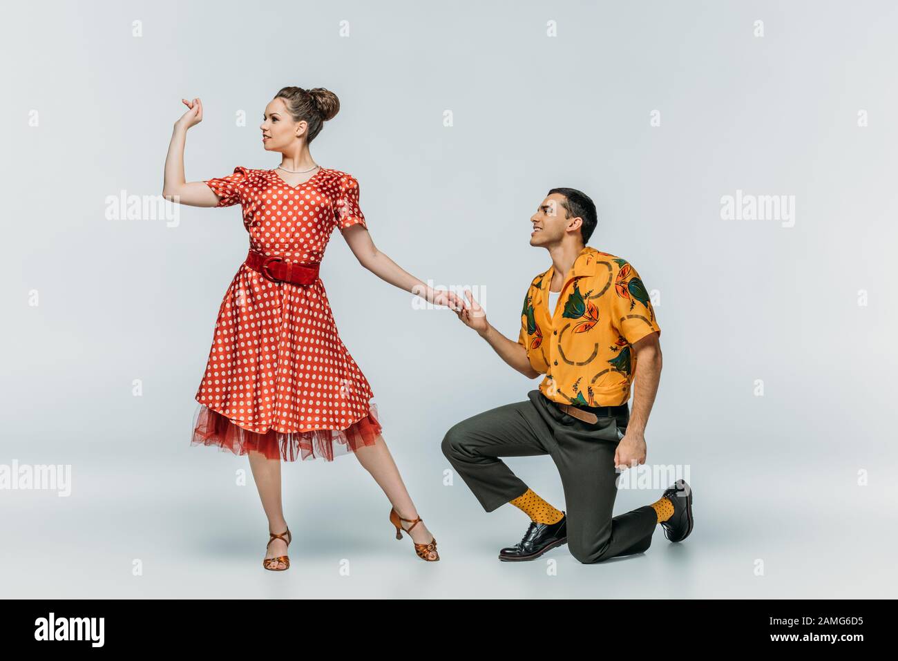 bell'uomo in piedi sul ginocchio e invitante bella donna per ballare boogie- woogie su sfondo grigio Foto stock - Alamy