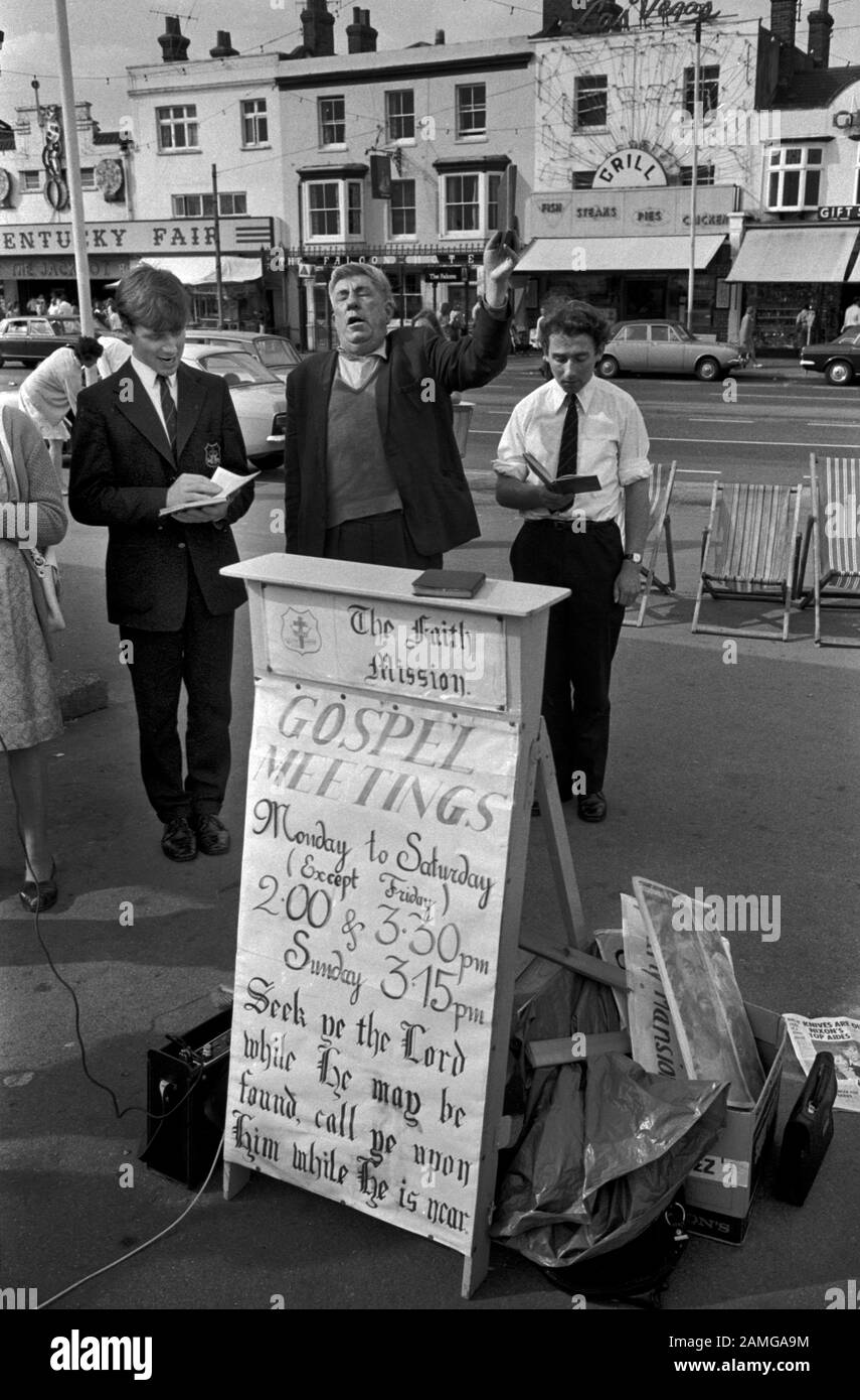 Predicatori di strada Regno Unito. Incontro cristiano evangelico di strada, uomini che tengono bibbie, mentre un'altra mano alzata chiama il Signore. Il cartello mostra i tempi degli incontri evangelici locali. "Cerca nel Signore, mentre egli si trova, invocalo mentre è vicino". Southend on Sea, Essex, Inghilterra. HOMER SYKES anni '1974 1970 Foto Stock