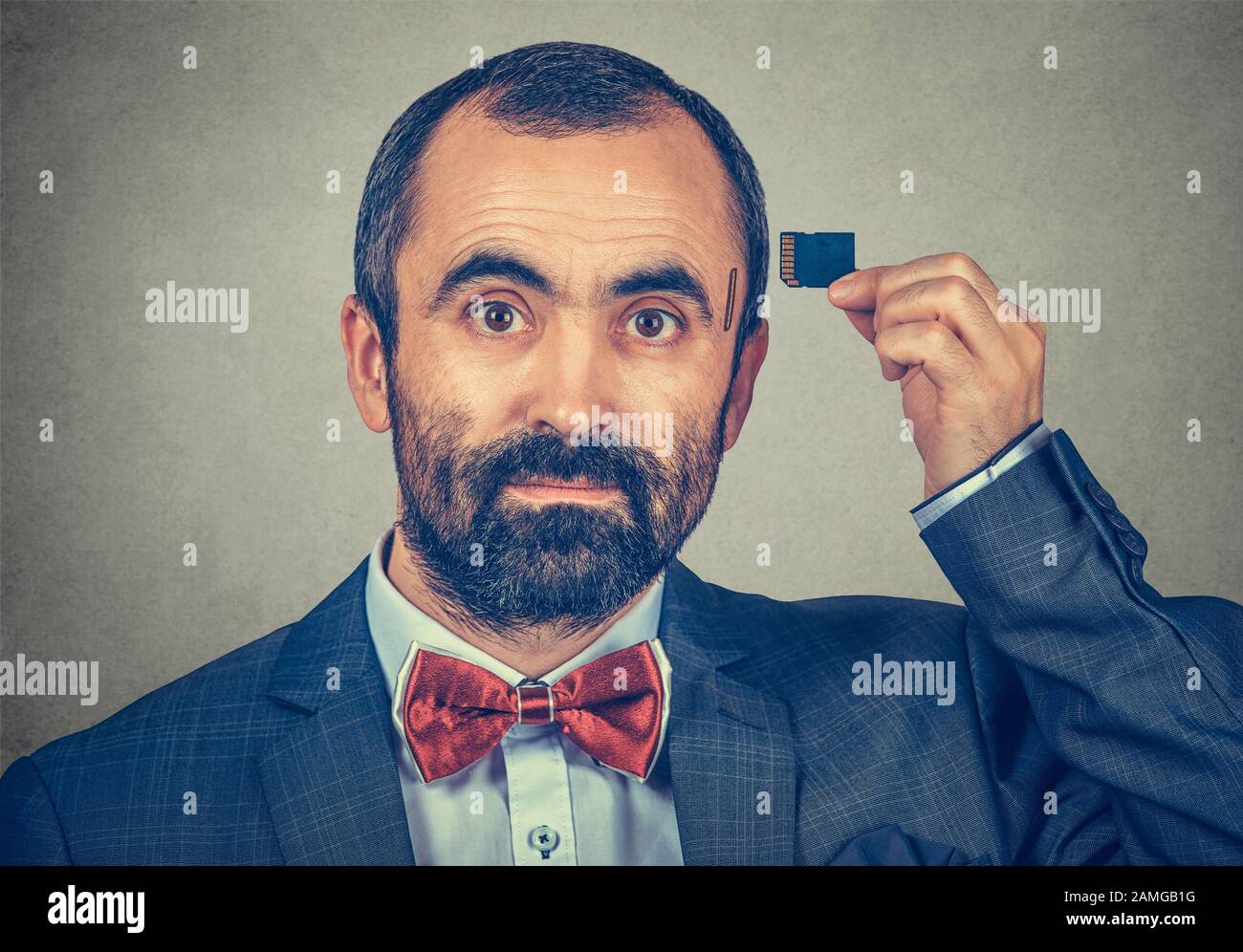 Memoria esterna necessaria. Ritratto di un serio uomo d'affari con una giacca elegante e cravatta rossa di prua che tiene la scheda Micro SD vicino alla sua testa i. Foto Stock