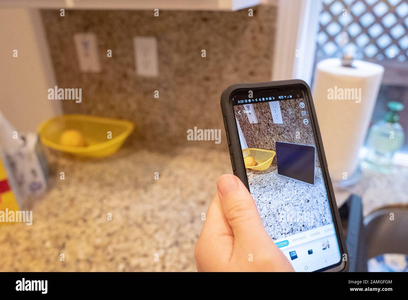 Mano di un uomo che tiene uno smartphone e utilizza le funzionalità di Realtà aumentata nell'app per lo shopping Amazon per visualizzare un dispositivo Amazon Echo Show su un bancone della cucina, San Ramon, California, 22 novembre 2019. La AR viene sempre più utilizzata come caratteristica per i consumatori per visualizzare i prodotti nelle loro case prima di prendere una decisione di acquisto. () Foto Stock