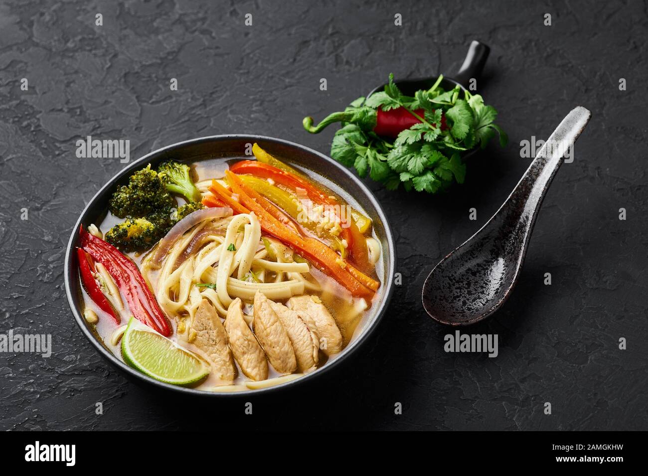 Pollo Thukpa in ciotola nera su fondo scuro di ardesia. Il pollo Thukpa è una zuppa di noodle di cucina tibetana con verdure e carne di pollo. Foto Stock
