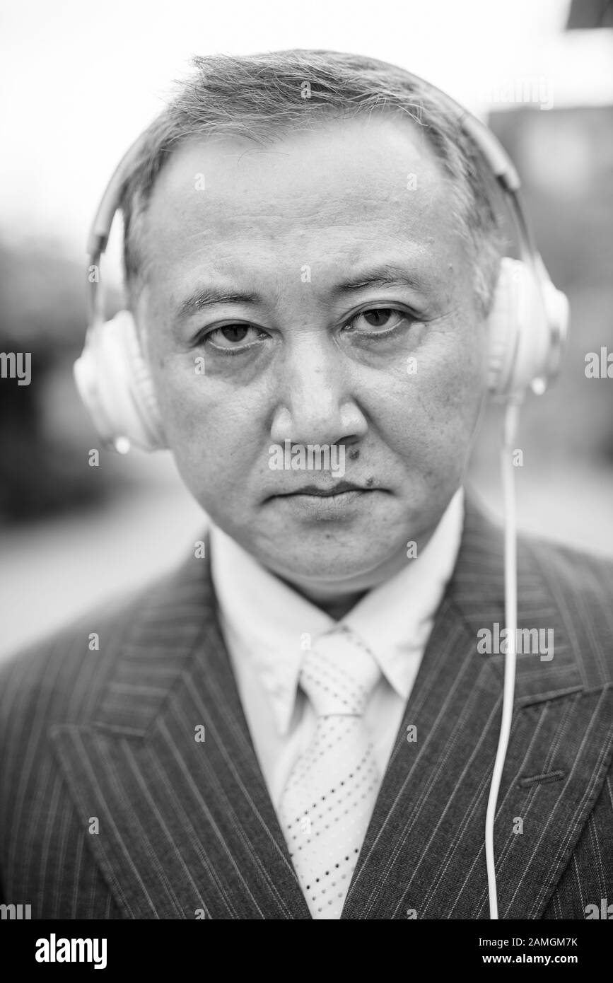 Ritratto di uomo d'affari asiatico maturo indossando il vestito mentre ascolta la musica nelle strade all'aperto Foto Stock