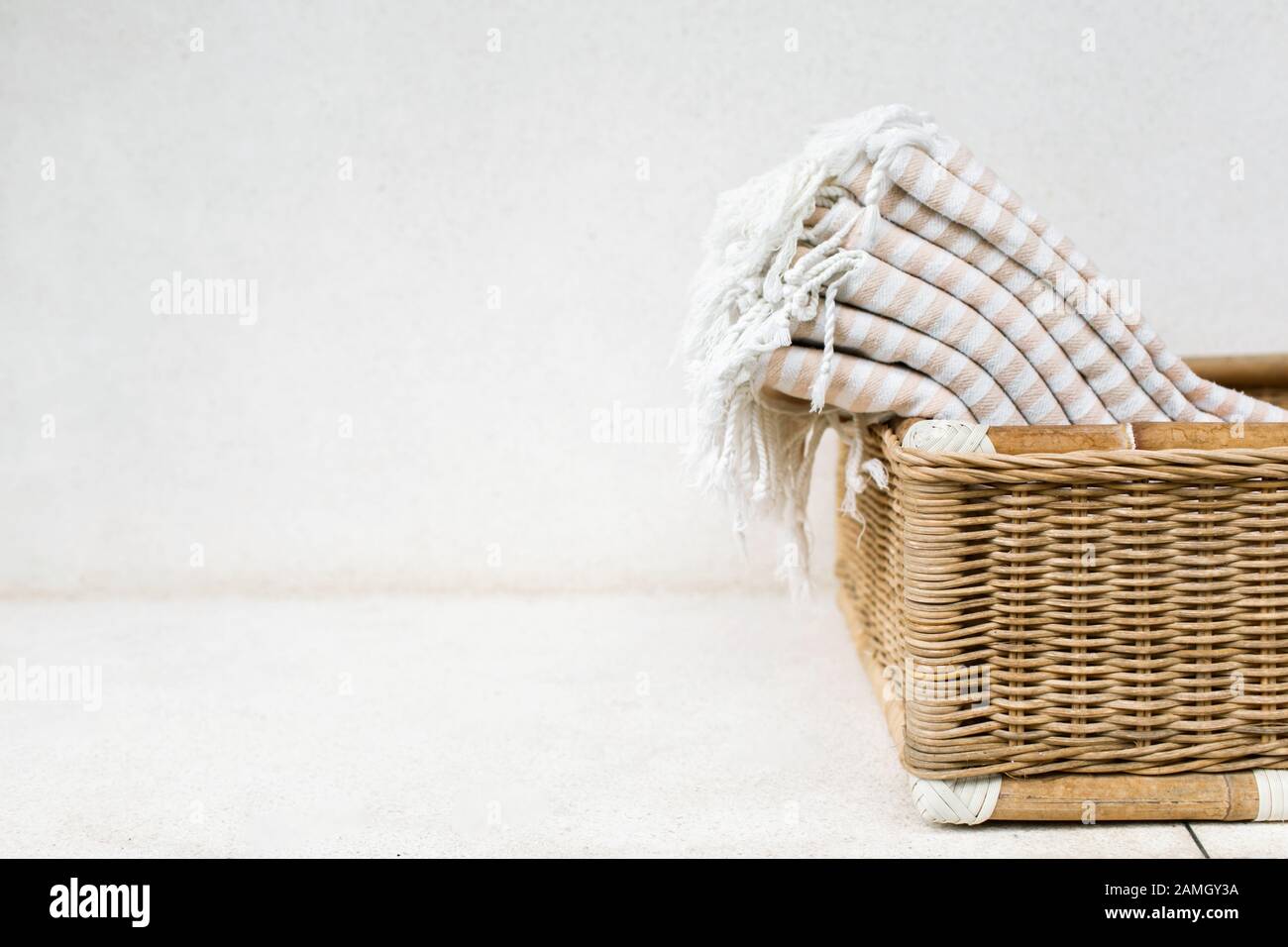 Asciugamani da bagno in cotone a strisce bianche giacenti in un cesto in vimini su sfondo bianco. Asciugamani organici a base di materiali naturali ecologici. Foto Stock