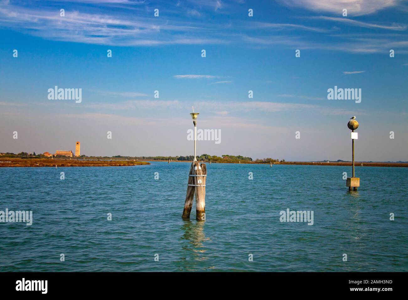 Colonne in legno in acqua segnano la via della nave tra le isole di Burano, Murano e Venezia, Italia. Il gabbiano è seduto sul pilastro. Foto Stock