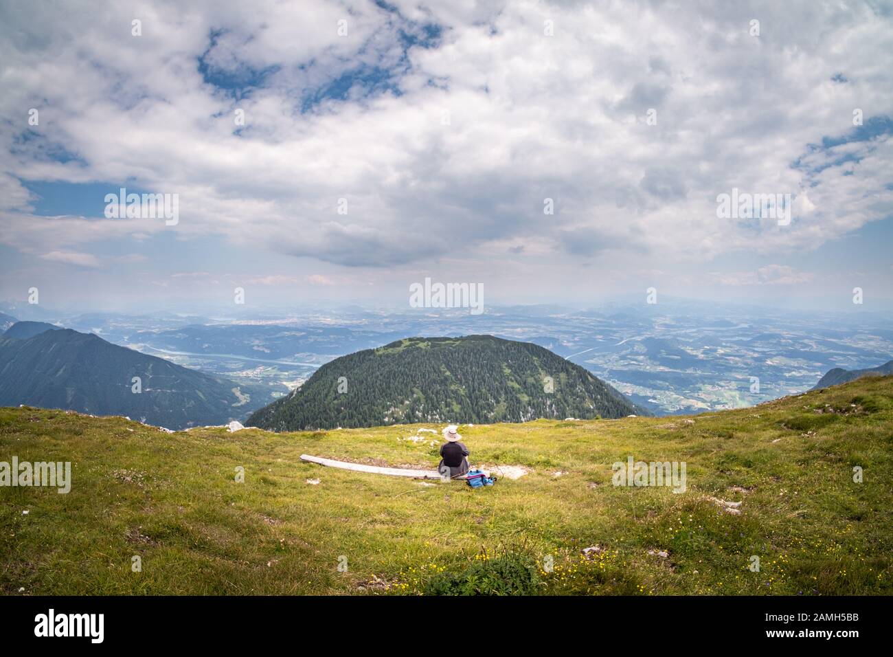 Vista dalla cima della montagna Hochobir con donna su panchina di legno che guarda alla montagna Kleinobir e valle Jauntal in Carinzia, Austria Foto Stock