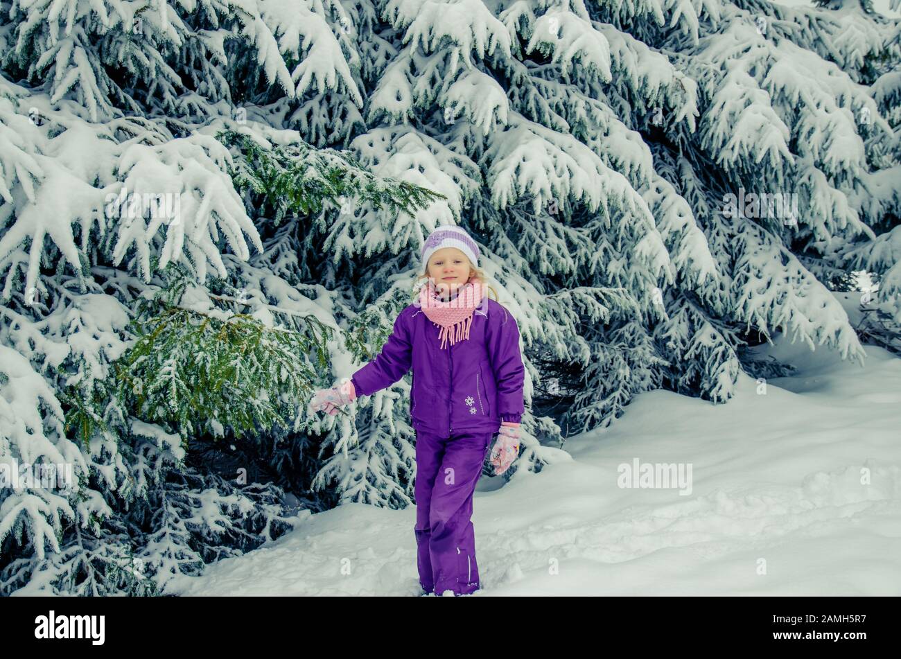 bella bambina sotto gli alberi coperti di neve nella magica natura invernale Foto Stock