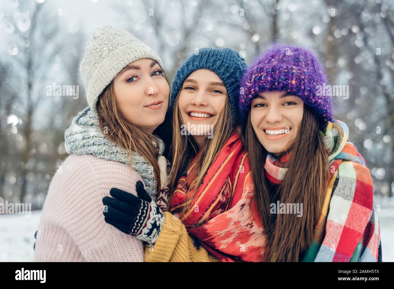 Tre amici donne all'aperto in cappelli a maglia divertirsi con un clima freddo nevoso. Gruppo di giovani amici femminili all'aperto nel parco invernale. Foto Stock