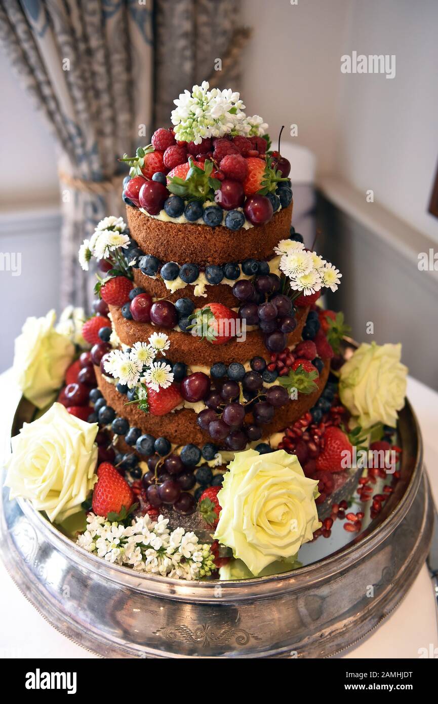 Torta nuziale nuda a livelli con frutta, frutti di bosco e fiori nel grande giorno del matrimonio. Foto Stock