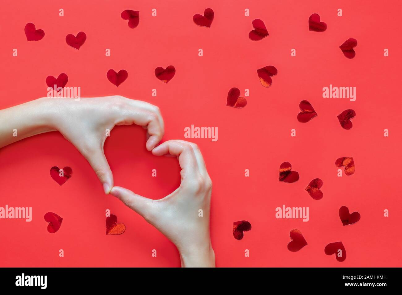 Le mani della donna che fanno la figura del cuore sullo sfondo rosso con i cuori rossi Foto Stock