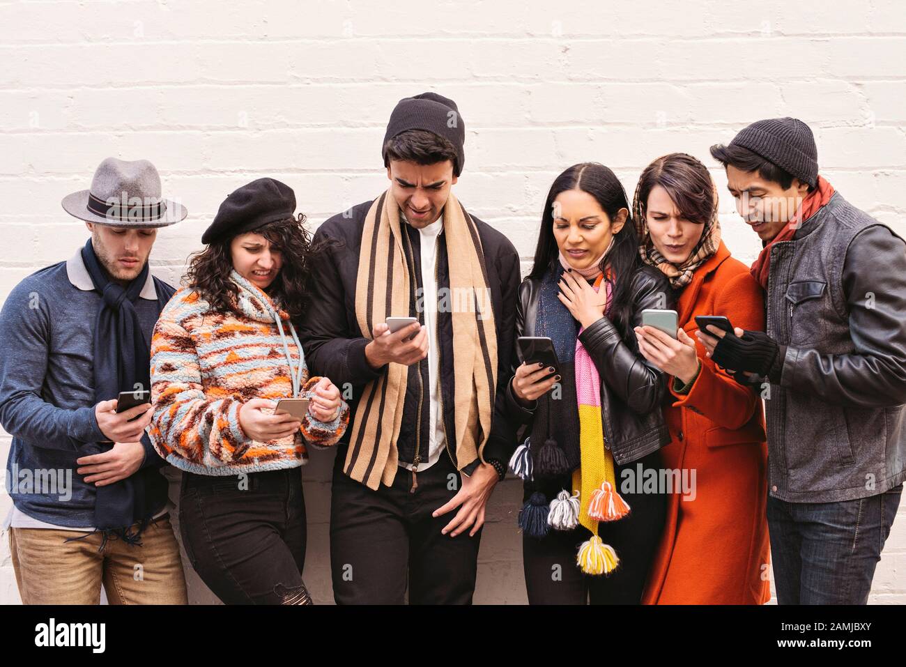 I giovani amici guardano in disgusto ai loro smartphone - diversità - Vestiti di abbigliamento invernale durante il giorno Foto Stock