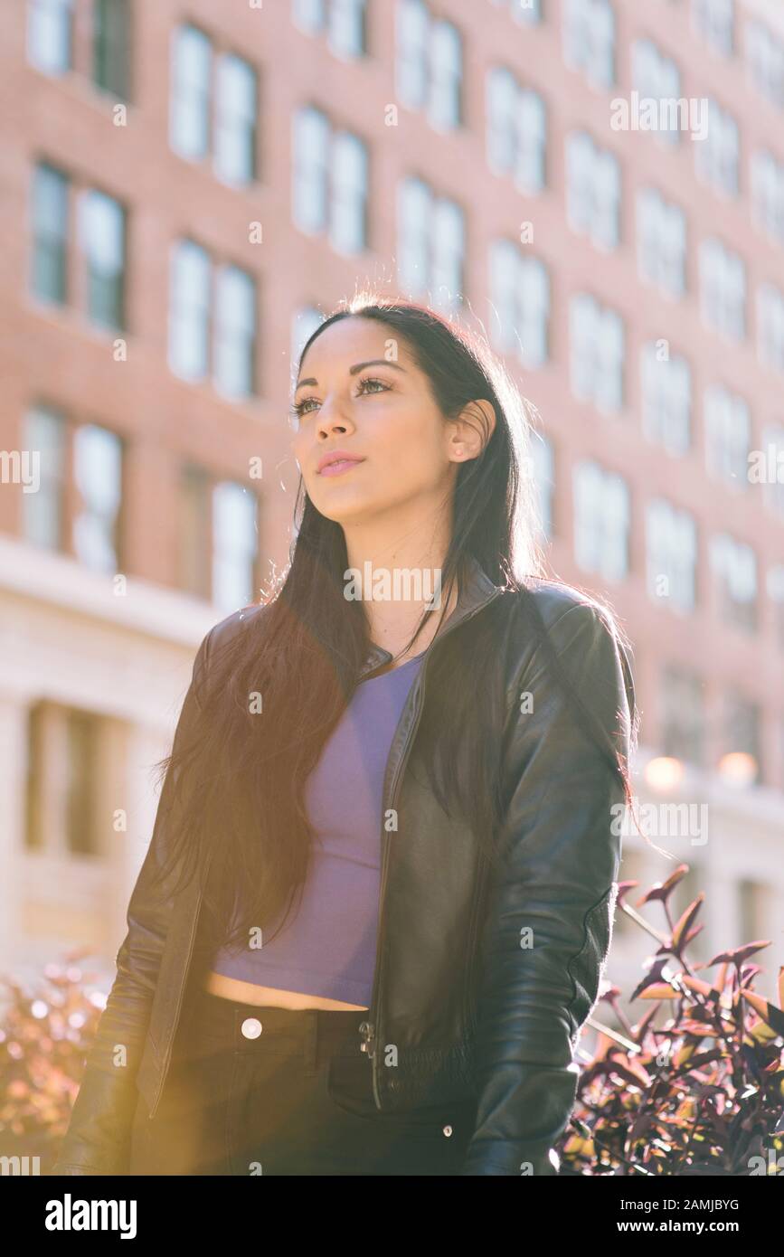 Latina femminile guarda ottimisticamente davanti a un edificio in città - Warm Lighting - Moda Foto Stock
