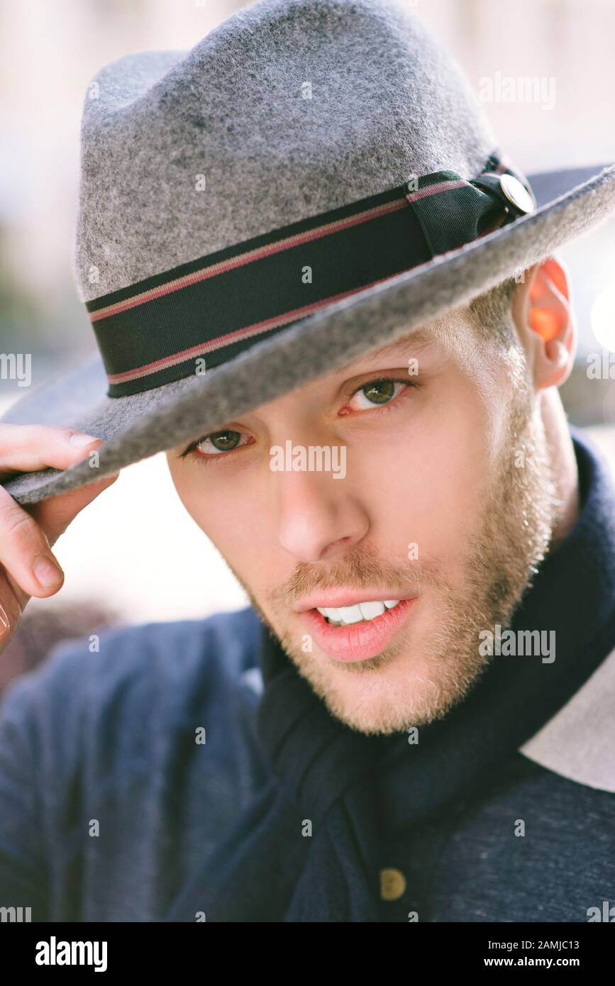 Uomo millenario guarda la macchina fotografica mentre mette una mano sul suo cappello - Moda - maschio bianco Foto Stock