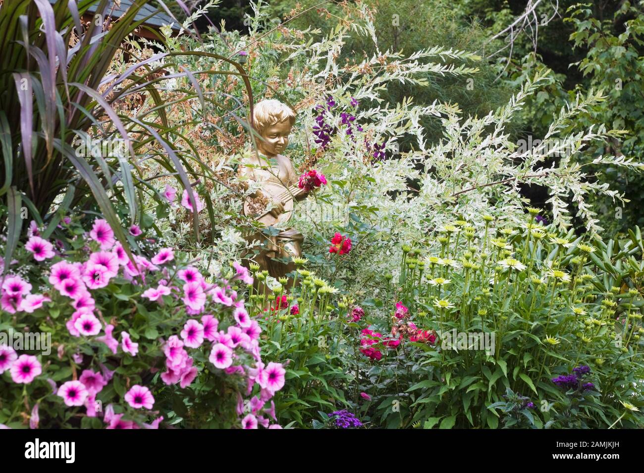 Statua dipinta in oro di giovane ragazzo che gioca un mandolino al confine con rosa Petunia x ibrida 'Easy Wave Plum Vein' fiori, rosso Rosa - Roses e Salix. Foto Stock
