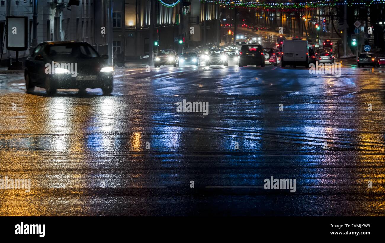 automobili che guidano nella strada notturna della città dopo la pioggia pesante Foto Stock