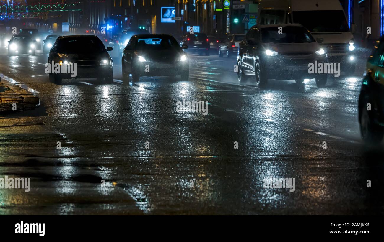 automobili che guidano nella strada notturna della città dopo la pioggia pesante Foto Stock