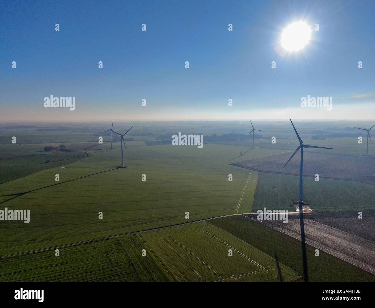 Vista aerea delle turbine eoliche nei campi agricoli durante il giorno invernale blu. Produzione di energia con energia pulita e rinnovabile. Foto Stock