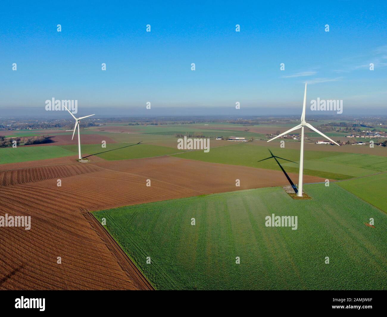 Vista aerea delle turbine eoliche nei campi agricoli durante il giorno invernale blu. Produzione di energia con energia pulita e rinnovabile. Foto Stock