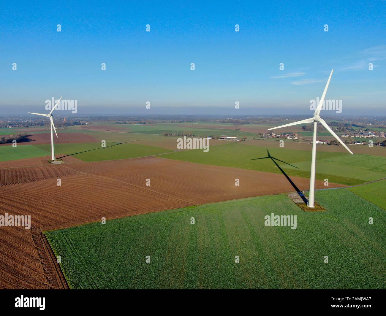Vista aerea delle turbine eoliche nei campi agricoli durante il giorno invernale blu. Produzione di energia con energia pulita e rinnovabile. Foto Stock