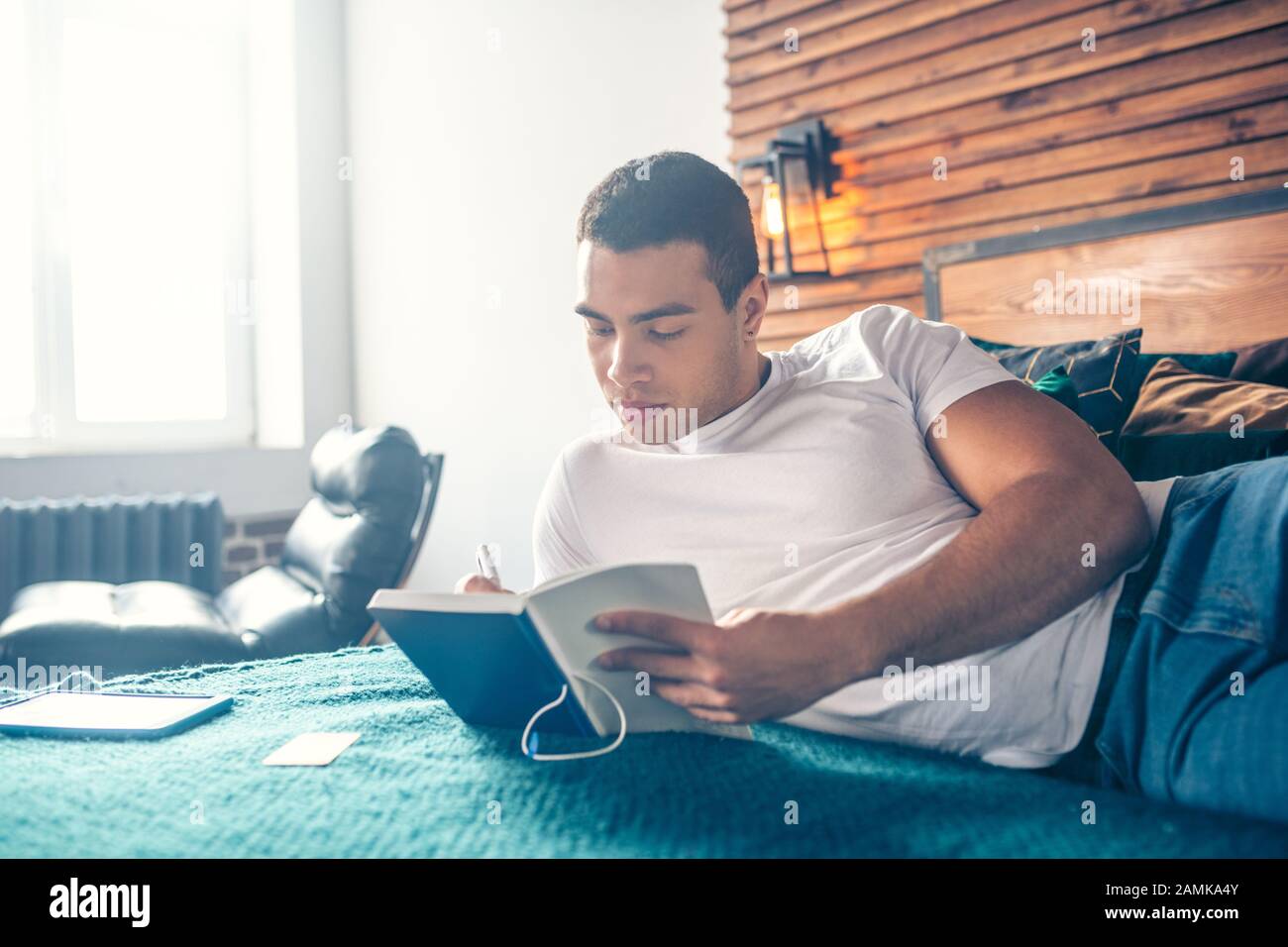 Guy scrivere esercizi in un notebook mentre sdraiato su un letto. Foto Stock