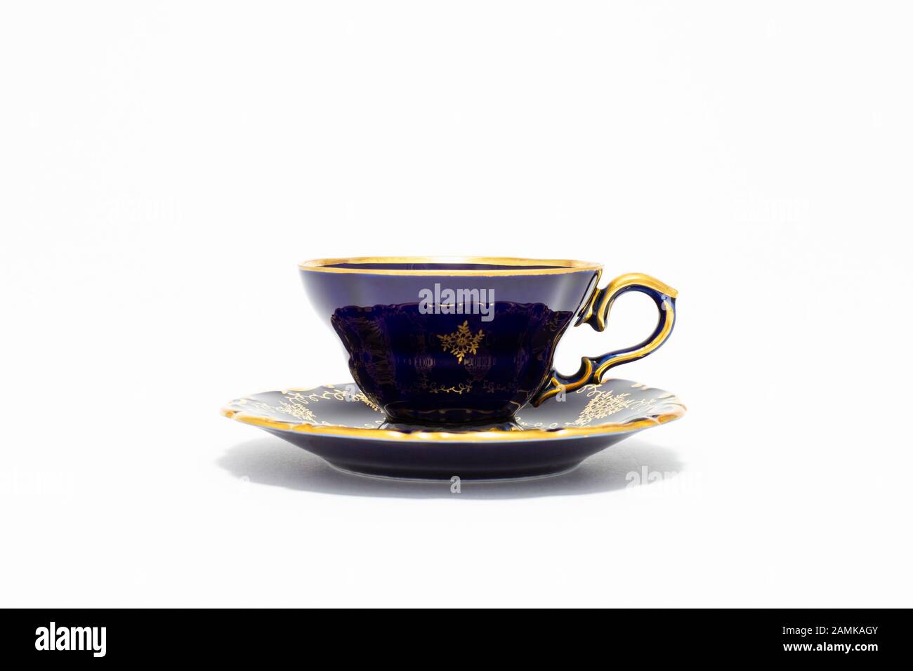 Closeup di una bella tazza di tè in porcellana vintage color cobalto blu con motivi floreali dorati su sfondo bianco Foto Stock