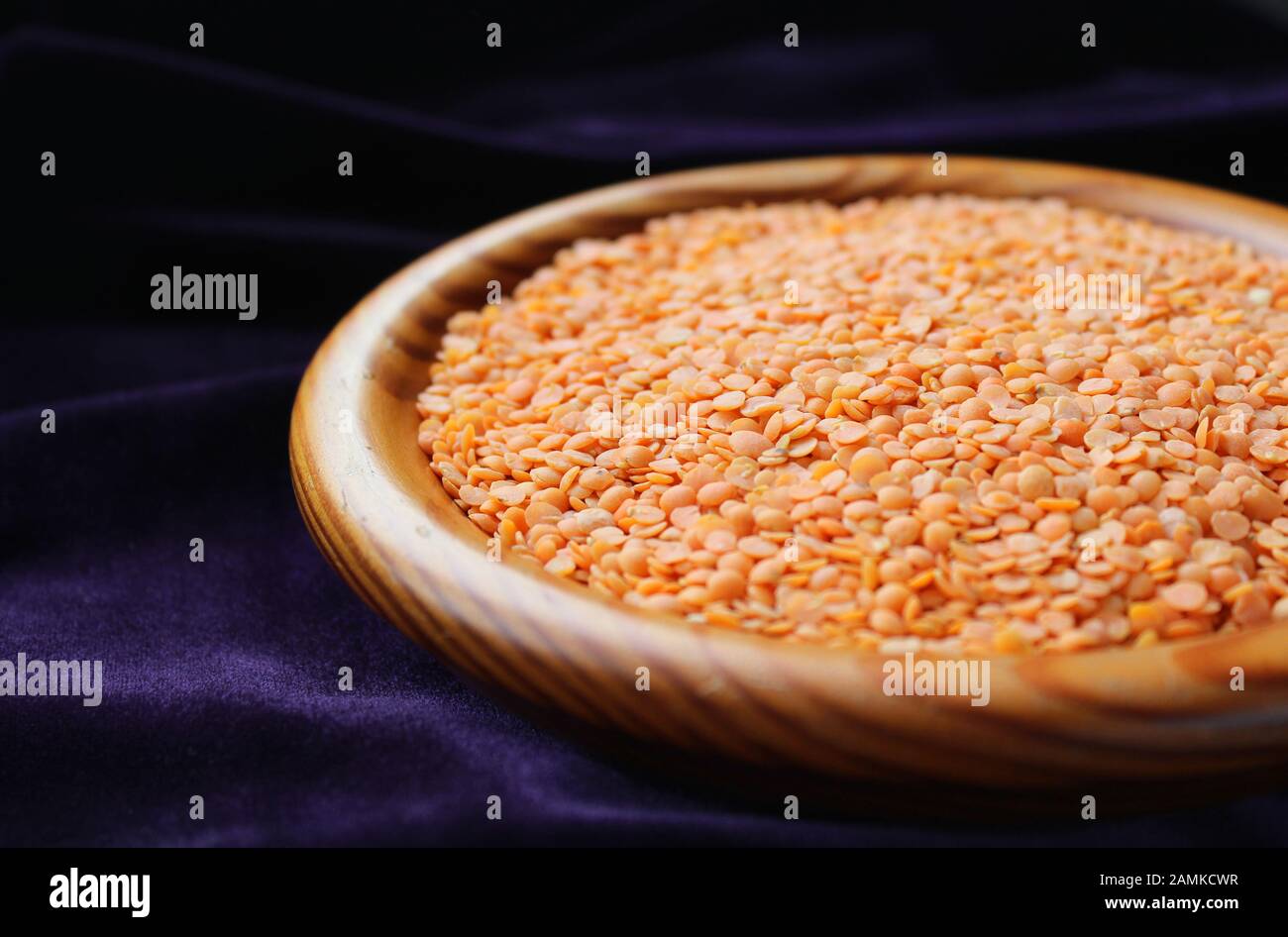 Primo piano di una ciotola di legno contenente lenticchie rosse, (Lens culinaris) contro un backgroound scuro, con spazio di copia. Messa a fuoco selettiva. Foto Stock