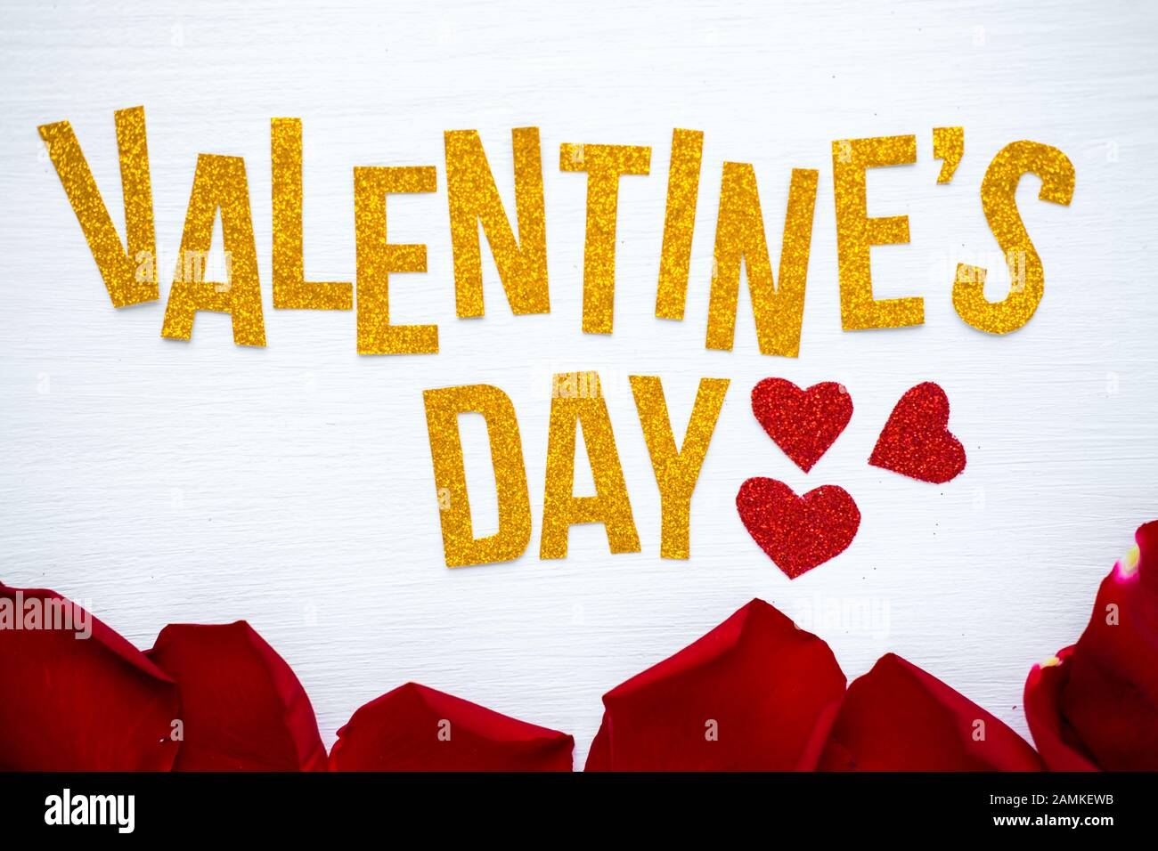 Happy Valentines Day text biglietto di auguri con petali di rosa rossa e sfondo di legno bianco di cuore. Concetto romantico e d'amore Foto Stock